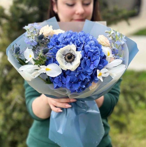 A close-up view of the "Enchanted Garden Symphony" bouquet, showcasing a captivating mix of hydrangeas, anemones, irises, eryngium, delphinium, and delicate spray flowers in full bloom, radiating the charm of an enchanted garden.