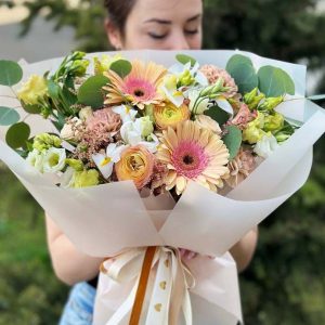 A vibrant and colorful bouquet featuring gerbera daisies, ranunculus, lisianthus, irises, astilbe, dianthus, and eucalyptus, arranged in a beautiful floral display.