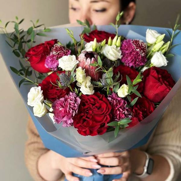 A captivating bouquet featuring protea, roses, lisianthus, scabiosa, eryngium, and eucalyptus, creating an exquisite blend of exotic and classic beauty.