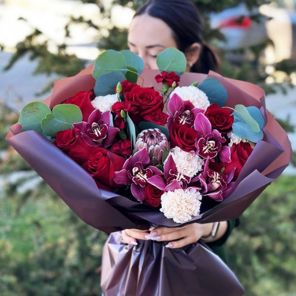 An enchanting bouquet showcasing roses, protea, dianthus, orchids, and eucalyptus. Perfect for romantic gestures and special occasions, radiating love and enchantment.