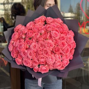 A beautifully arranged bouquet titled "Melody of Tenderness," featuring bright coral spray roses, elegantly wrapped in dark grey paper.