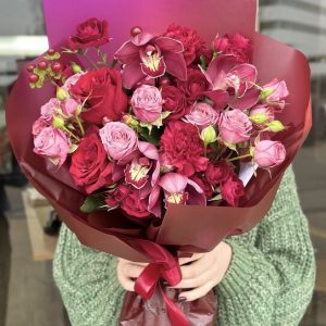 A lush bouquet featuring vibrant red carnations, luxurious orchids, classic red roses, and charming red spray roses, creating a romantic and elegant arrangement perfect for special occasions.