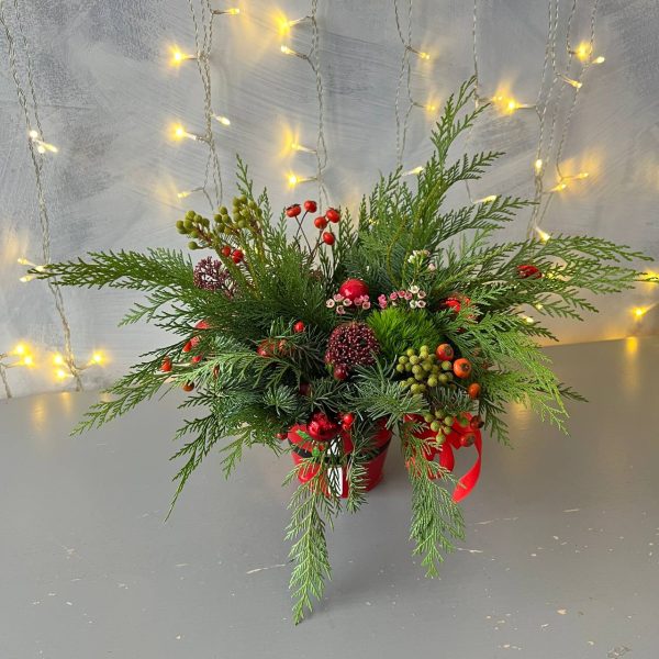 Christmas floral arrangement "Winter's Embrace" featuring lush greenery with red accents.