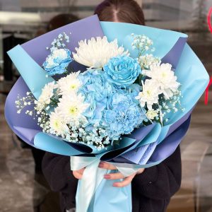 Flower arrangement with blue hydrangeas, blue roses, and white chrysanthemums, showcasing elegance and serenity.