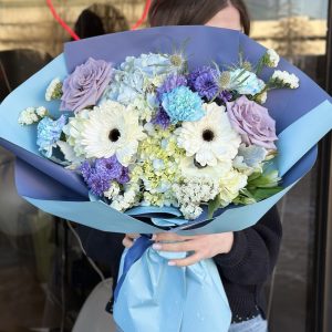 A beautiful floral arrangement named "Elysian Bloom," featuring vibrant Gerberas, lavender roses, soft hydrangeas, delicate carnations, and unique eryngium, creating an elegant and ethereal display.