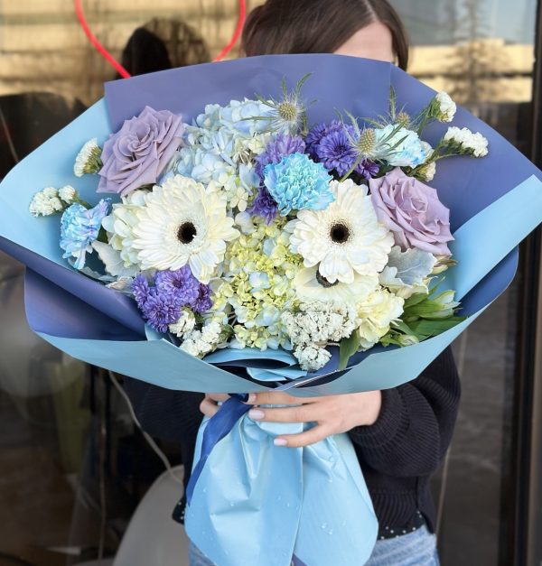 A beautiful floral arrangement named "Elysian Bloom," featuring vibrant Gerberas, lavender roses, soft hydrangeas, delicate carnations, and unique eryngium, creating an elegant and ethereal display.