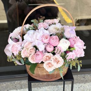 Floral basket with spray roses, hydrangeas, chrysanthemums, and roses in soft pastel colors, arranged in a woven basket.