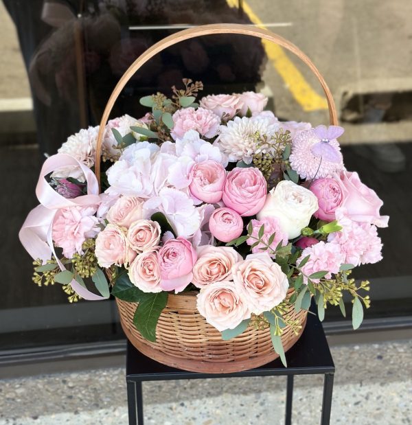 Floral basket with spray roses, hydrangeas, chrysanthemums, and roses in soft pastel colors, arranged in a woven basket.
