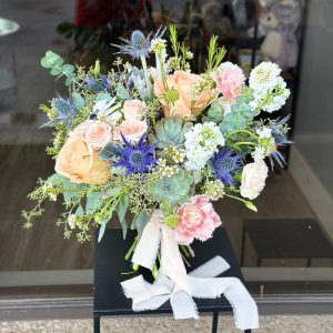 Bridal bouquet with mix of roses, carnations, eryngium, fresh greenery, and unique seasonal blooms