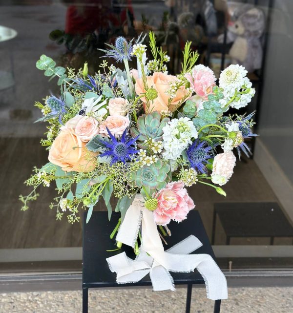 Bridal bouquet with mix of roses, carnations, eryngium, fresh greenery, and unique seasonal blooms